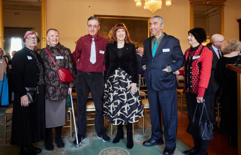 A group of five people are standing in a line. They are facing the camera and posing for a photo.